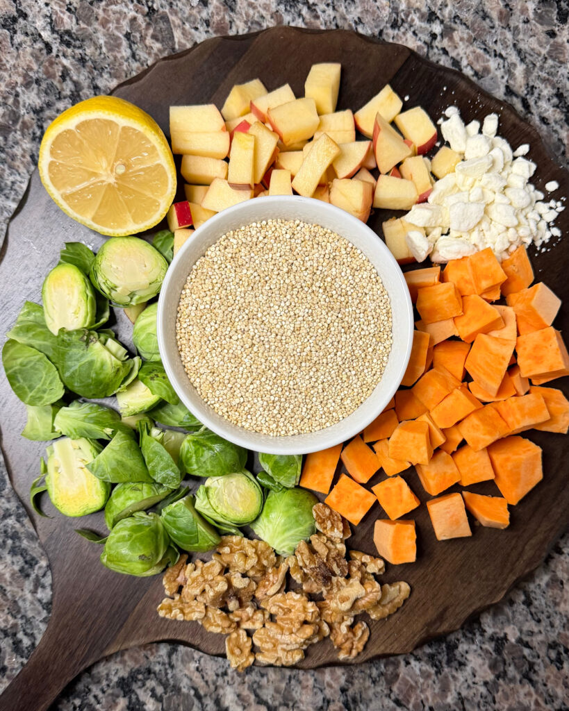 Quinoa, sweet potatoes, Brussels sprouts, chopped apple, walnuts, cheese, and lemon arranged on a wooden board