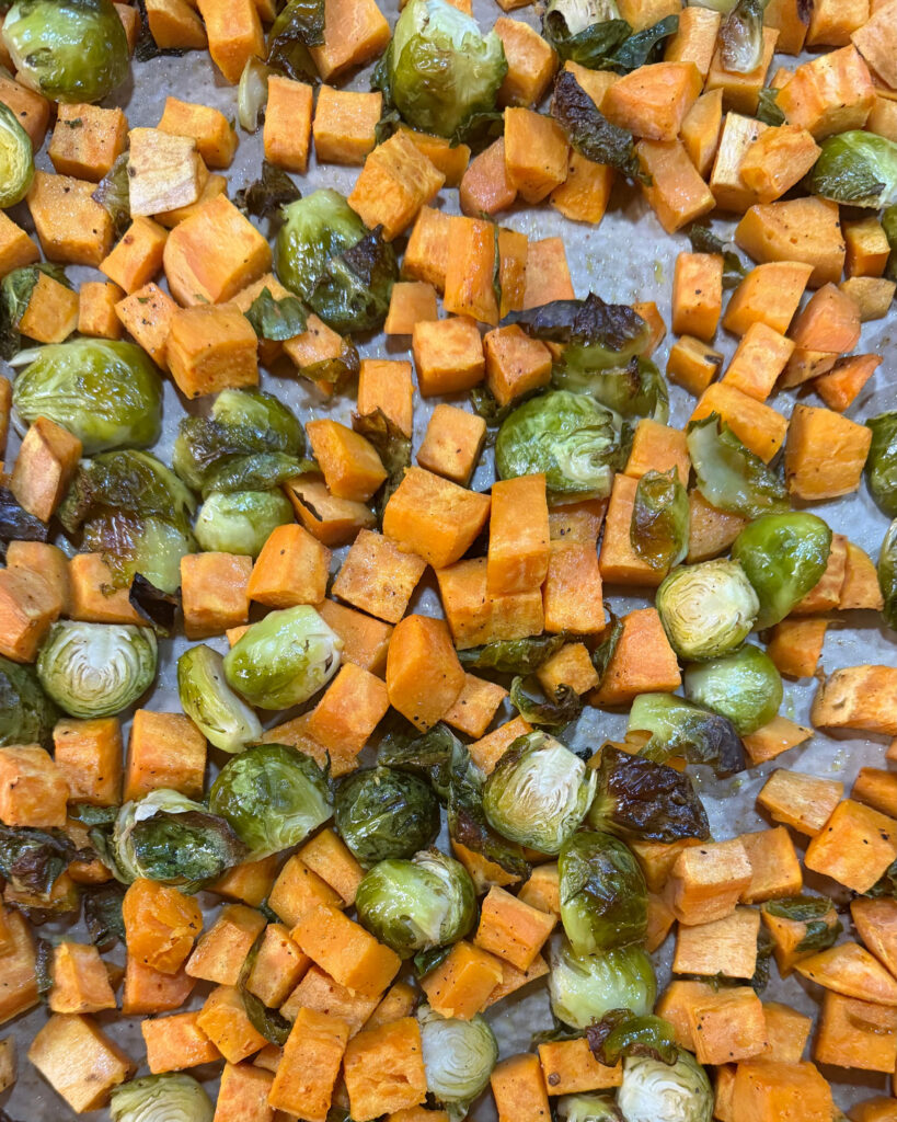 Roasted sweet potato cubes and Brussels sprouts with browned edges on a parchment-lined baking sheet